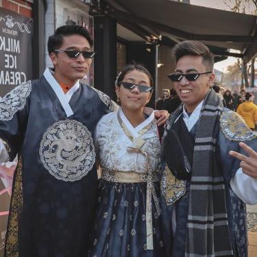 3名学生穿着传统的中国服装，戴着像素太阳镜，在繁忙的街道上摆姿势拍照.
